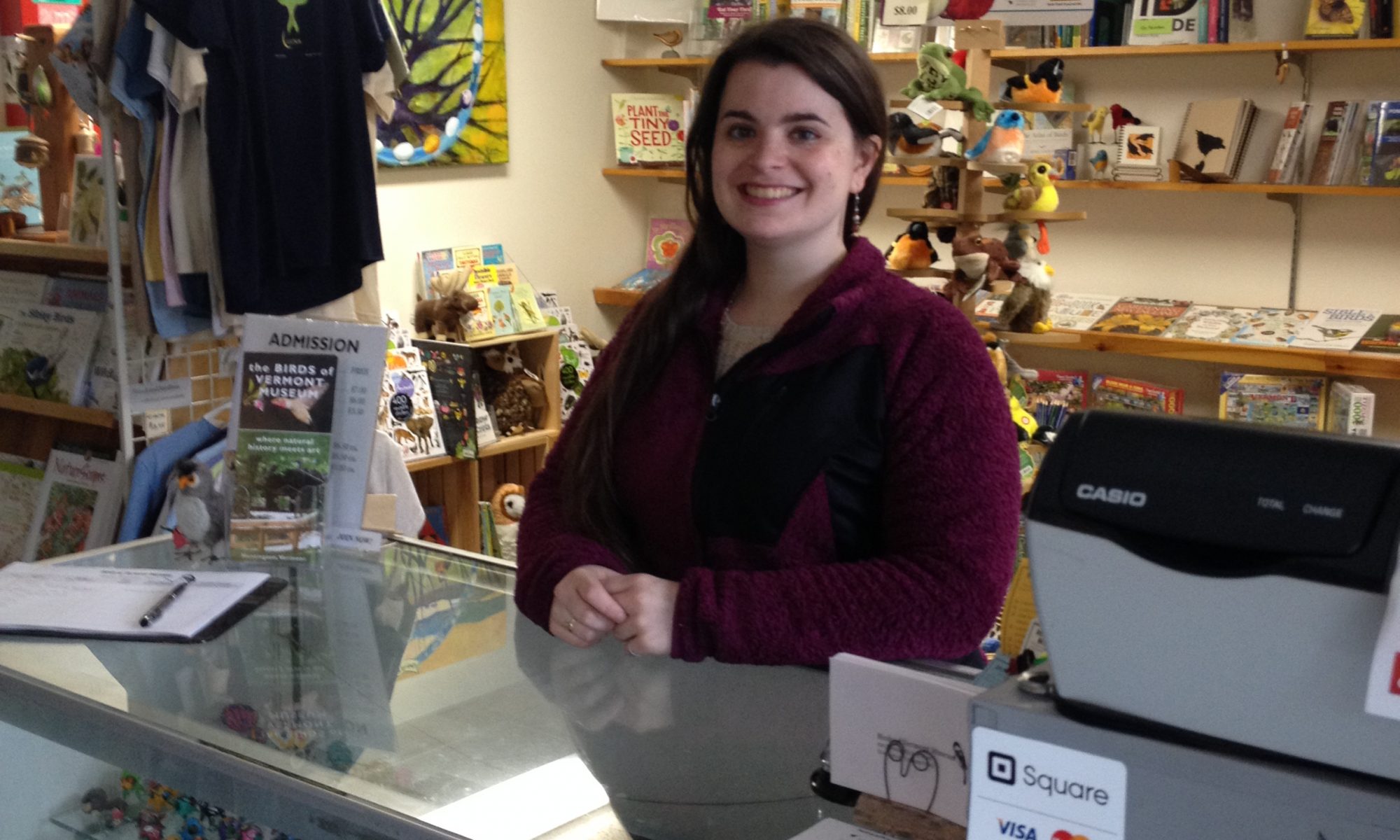 A smiling woman at the Museum's front desk with the gift shop behind her.