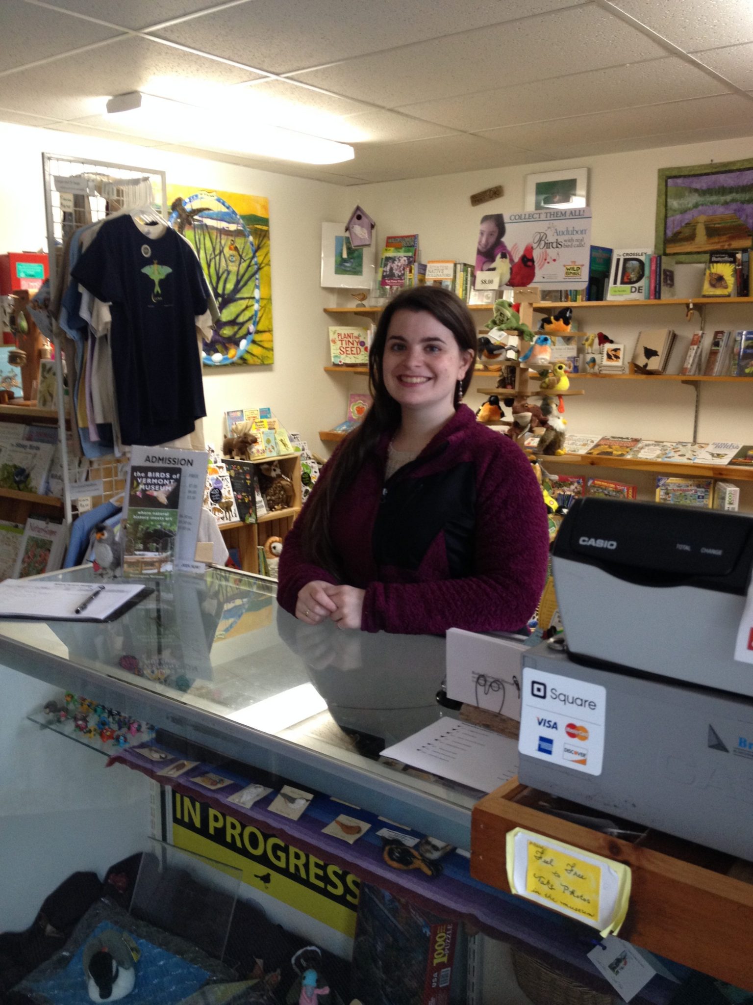 A smiling woman at the Museum's front desk with the gift shop behind her.