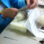 making a felted owl: Work In Process 2 (wrapping soft gray wool around wool body; work is on a plastic-protect foam pad to protect needles and work surface)