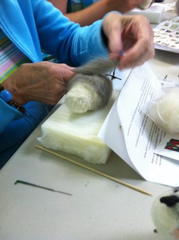 making a felted owl: Work In Process 2 (wrapping soft gray wool around wool body; work is on a plastic-protect foam pad to protect needles and work surface)