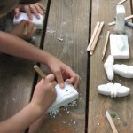 Child (hands and part of torso) carving a white bar soap using a craft-stick tool.