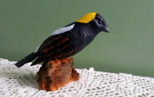 Simplified woodcarving of a bird, painted to match Bobolink plumage. Woodcarving is on a small base resting on a lace tablecloth. Carving and photo by Dave Tuttle, shown by permission.
