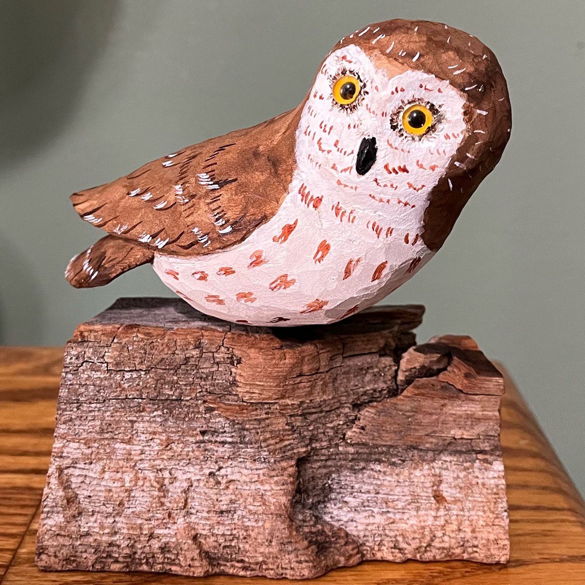 saw-whet owl carved in wood and painted, perched on a chunk of wood with bark on it