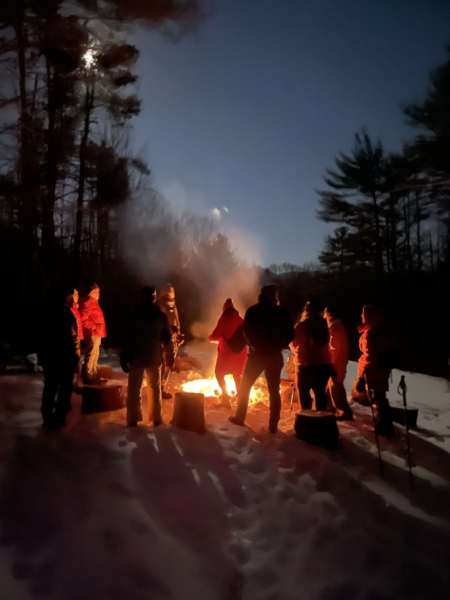 People surround an outdoor fire on a snowy full moon night