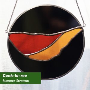 A stained glass disk with black and top and bottom, and a bowl-like shape of red and orange spanning the disk, offset towards the top. There are two small chains attached at the side to suspend the disk against a pale background. Title: Conk-la-ree! Art by Summer Stratton. Copyright © 2024 and used with permission. 